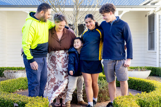 Portrait of mixed ethnicity family standing on brick pathway in front of white house