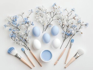 A flat lay composition featuring pastel blue and white Easter eggs, delicate floral branches, and painting brushes with a small can of blue paint.