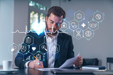 Calm businessman in formal wear signing contract at office workplace with coffee cup, laptop and notebook. Concept of successful deal, agreement, partnership, documents. Medical healthcare icons.