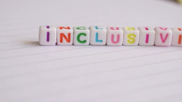 Inclusivity, a word formed with white and colored blocks on a lined sheet, and a hand joining the last letter