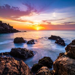 Naklejka premium A coastal sunset displays radiant colors. The water blurs across the rocks, reflecting the sun's warm glow and creating a serene scene