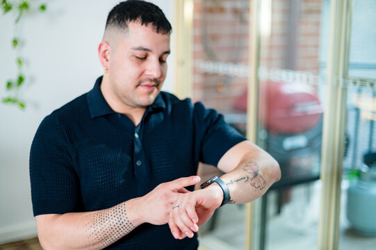 Men's style and technology blend as he engages with a smart watch in a modern living space.