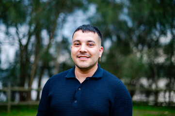 A man in his 30s stands in a park, smiling brightly while enjoying the day outdoors