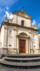 Obraz premium Cream facade of a quaint church with steps leading to the wood doors, under a blue sky