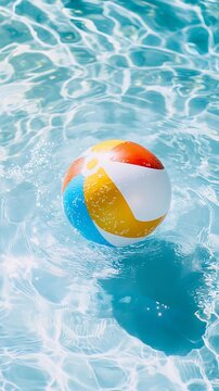 Colorful beach ball gently floating in shimmering blue swimming pool water on a bright summer day, leisure.