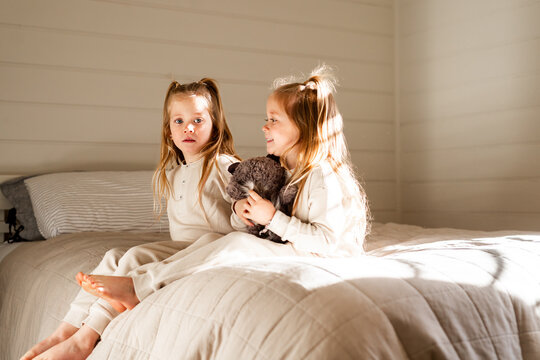 Twin girls holding raccoon toy sitting on the bed