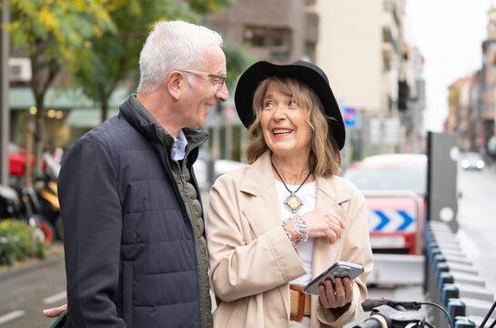 Portrait of happy senior couple talking and smiling while using smartphone for bike sharing