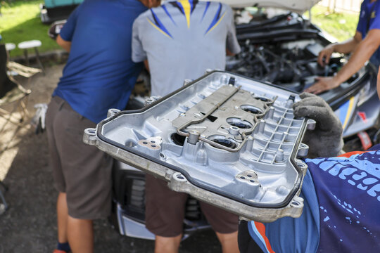 Close up of mechanic holding cylinder head cover during car engine repair. Two focused men performing vehicle maintenance work in garage for automotive service