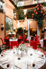 Elegant luxury restaurant interior with beautifully arranged round tables, red velvet chairs, white floral centerpieces, and refined table settings in a bright atrium dining hall.