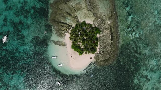 Small island with palm trees, white sand, turquoise water and boats anchored along the shore. Guyam Island. Siargao, Philippines.