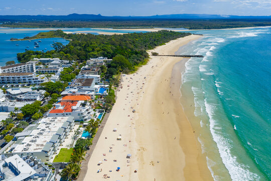 Aerial view of gentle waves on a white sandy beach covered in towels, umbrellas and sunshades