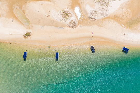 Aerial view of 4 small pleasure boats anchored in turquoise water off a coastal beach