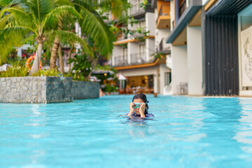 Naklejka premium summer Asian child wearing goggles to training dive in swimming pool or young kid girl playing water in waterpark or people learning swim sports exercise at school or holiday vacation travel at hotel