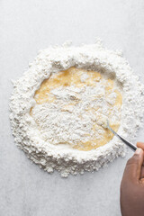 Overhead view of pasta dough being mixed on a white granite countertop, process of making homemade pasta dough