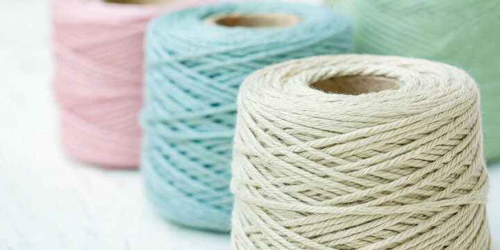 Close-up with shallow depth of field on a row of large spools of yarn or thread in soft pastel and muted colors (beige, blue, pink, mint green). Use for craft blogs, knitting tutorials, and textile 