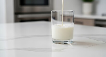 Milk pouring into a glass set on a marble countertop in a bright modern kitchen with blurred appliances in the background