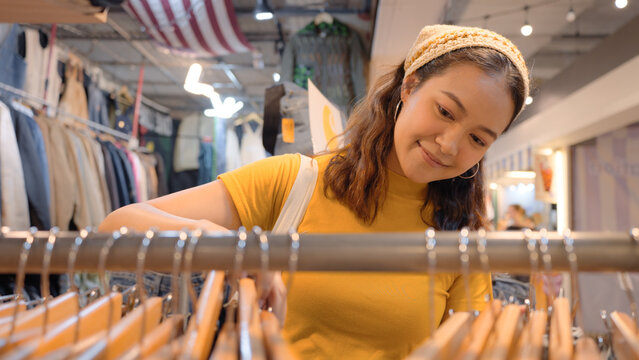 Young teen tourist Gen Z asia female choose look at zero waste eco go green buy second hand sale store flea market thrift old used vintage fabric style. Happy woman city asian people small retail shop