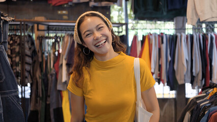 Young teen Gen Z asia female happy smile looking at camera at zero waste eco go green buy second hand sale store flea market mall thrift old used vintage fabric retro style. Woman people enjoy shop.