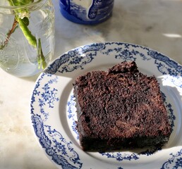 Coffee and chocolate cake with white rose in little vase on blue tableware with sunlight