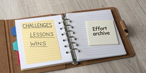 Organized notebook open showing sticky notes for challenges, lessons, and wins with a blank page for effort archive on wood surface