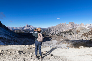 A senior traveler hikes alone along a mountain trail under bright sunlight, surrounded by stunning...