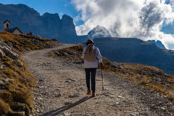 A senior traveler hikes alone along a mountain trail under bright sunlight, surrounded by stunning peaks and clouds, embracing freedom, wellness, and adventure in nature.