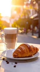 Croissant and latte on a table outdoors, bathed in golden morning sunlight