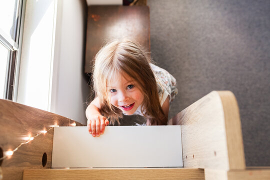 Happy little Australian girl with messy hair climbing up bunk bed ladder in her bedroom