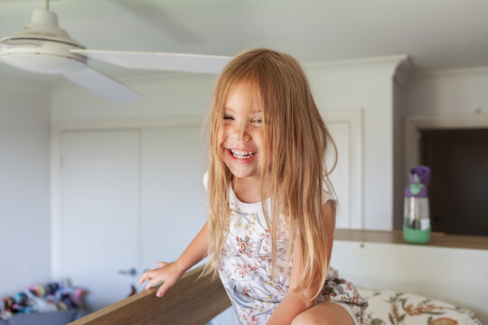 Happy little Australian girl with messy hair in her bedroom sitting on bunk bed in the morning