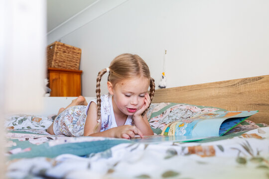 Little preschool aged child lying on bunk bed reading a storybook looking at pictures in bedroom