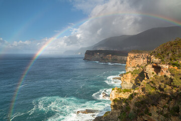 Elevated view of a double rainbow and dark storm clouds over rugged coastal cliffs
