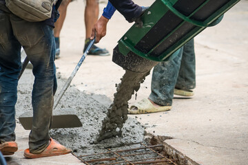Nonthaburi, Thailand - November, 07, 2025 : Construction workers pouring wet concrete from a truck chute and spreading it using tools for a pavement or foundation