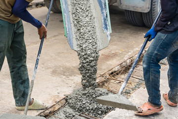 Nonthaburi, Thailand - November, 07, 2025 : Construction workers pouring wet concrete from a truck chute and spreading it using tools for a pavement or foundation