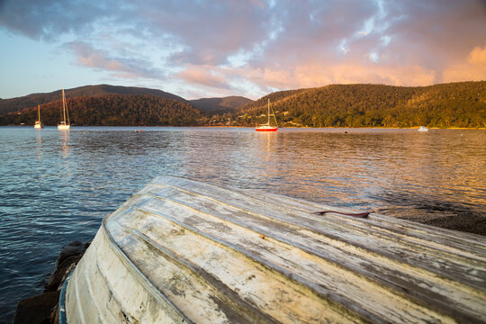 Boats on a coastal bay at sunset behind an upturned rowboat on the shore