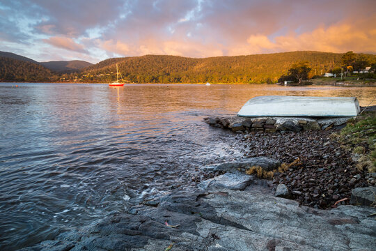 An upturned row boat on the waters edge of coastal bay under a colourful sunset sky