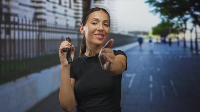 Young hispanic woman extends hand while holding a handgrip exerciser on a city street; confidence friendliness.