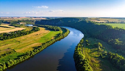 Fototapeta premium Expansive River Winding Through Lush Green Countryside Under a Clear Blue Sky with Soft Sunlight