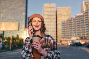 Fototapeta premium woman coffee phone smile urban beanie candid lifestyle portrait in golden hour glow, authenticity and mindful living captured with emotional storytelling in contemporary city street.
