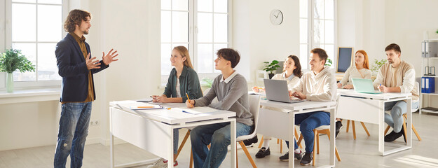 Male teacher leads lesson for group of teenage pupils or students in school classroom, focusing on learning and studying in a supportive setting with dedication and knowledge daily.