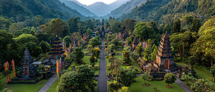 panoramic shot of multiple Balinese temples in Tampaksiring decorated for festival season, colorful penjor bamboo poles lining pathways, lush forests and hills surrounding the sacred site