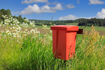 Red mailbox made of plastic by rural road on a beautiful day of summer. Copy space. 