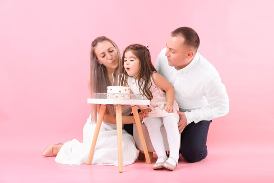 Birthday celebration. Happy family with tasty cake and daughter blowing out candles on pink background - Powered by Adobe