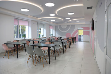 Tables with chairs in stylish room at school