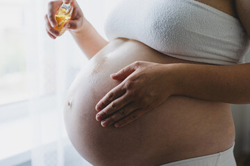 A pregnant woman applies skincare cream to her skin. This moment emphasizes self-care during pregnancy.