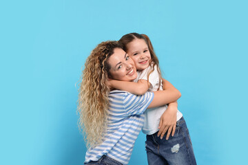 Happy mother hugging her daughter on light blue background. Family bonding