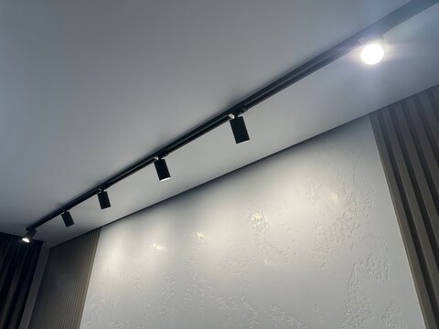 Stylish illuminated track lighting on white ceiling in room, low angle view