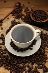 Aromatic coffee in cup and beans on wooden table, closeup