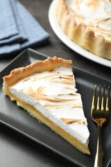 Slice of tasty lemon meringue tart served on black table, closeup