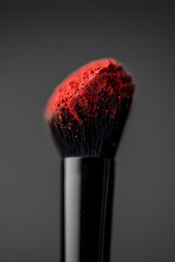 Soft makeup brush coated with vibrant red powder against a dark background