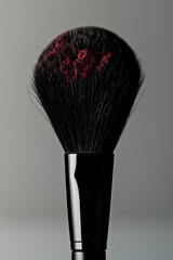 Soft makeup brush coated with vibrant red powder against a dark background